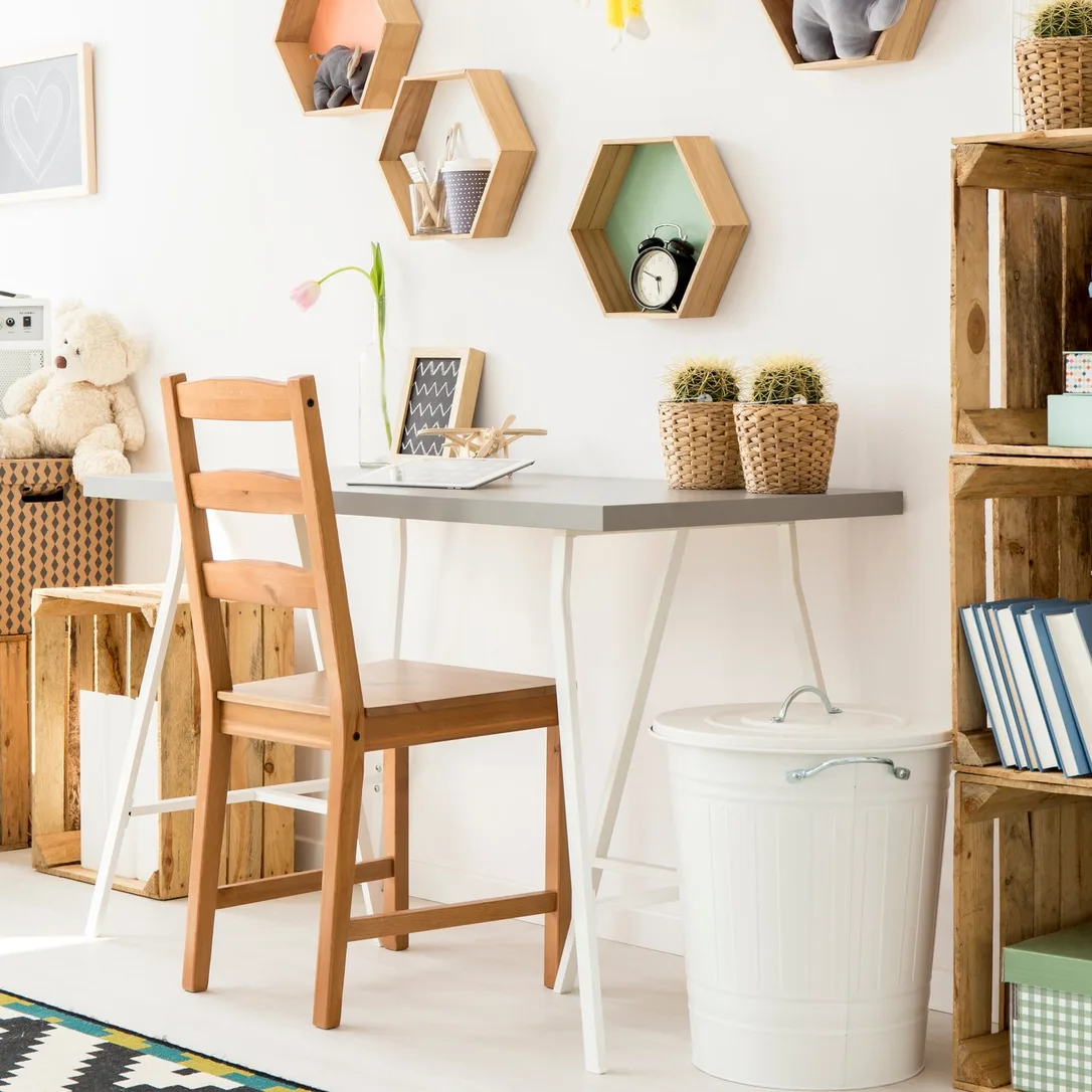 A narrow gray desk and wooden chair beneath small wooden hexagonal wall shelves.