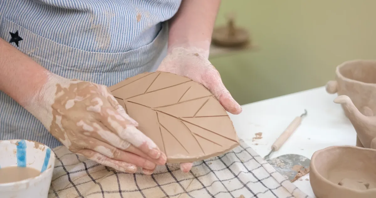 A hand refining a clay leaf edge while the shape is supported underneath.