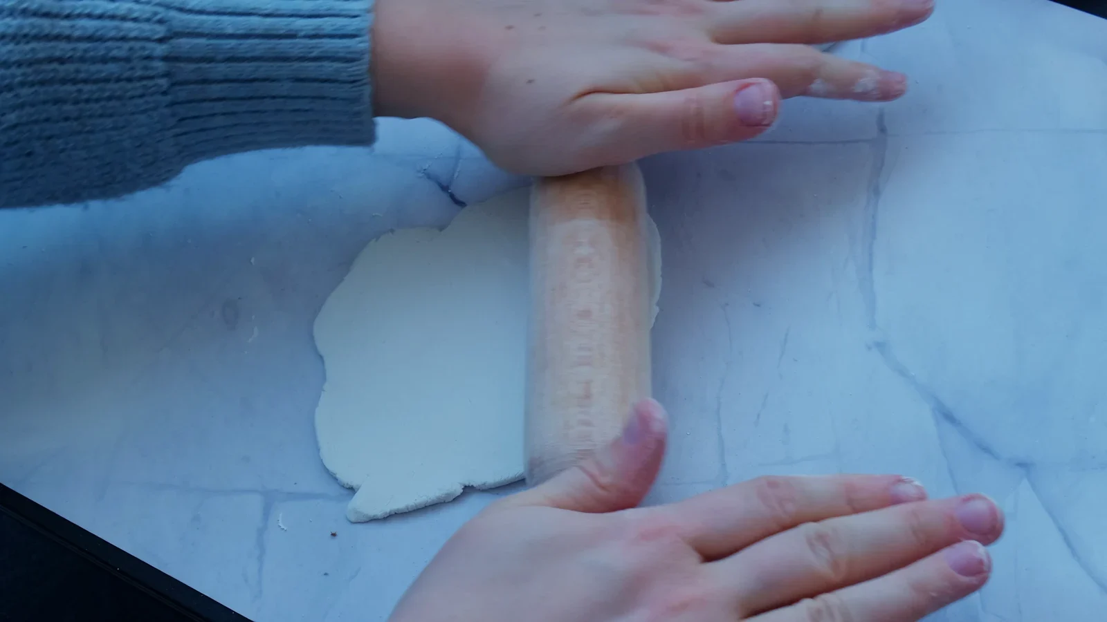 Rolling pin flattening a white clay sheet.