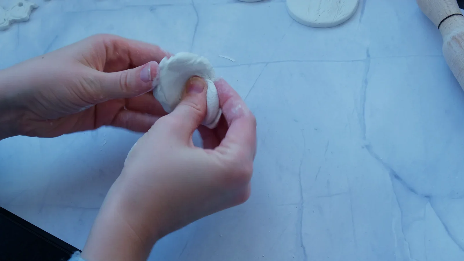 Hands softening white modelling clay on a smooth work surface.