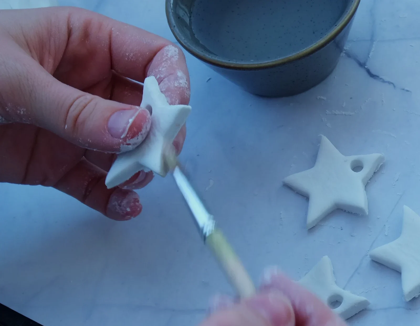 Hands and a brush refining the edges of a white clay star.